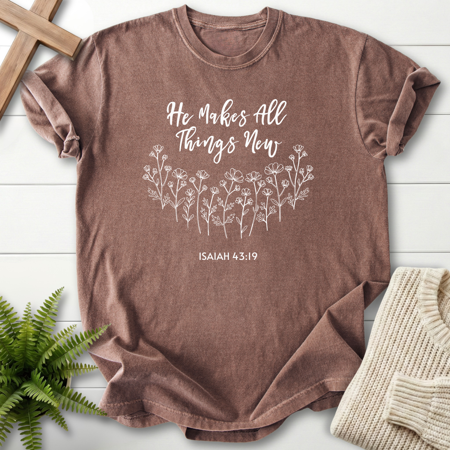 Espresso women's faith t-shirt with cursive 'He Makes All Things New' lettering and botanical wildflowers, inspired by Isaiah 43:19.