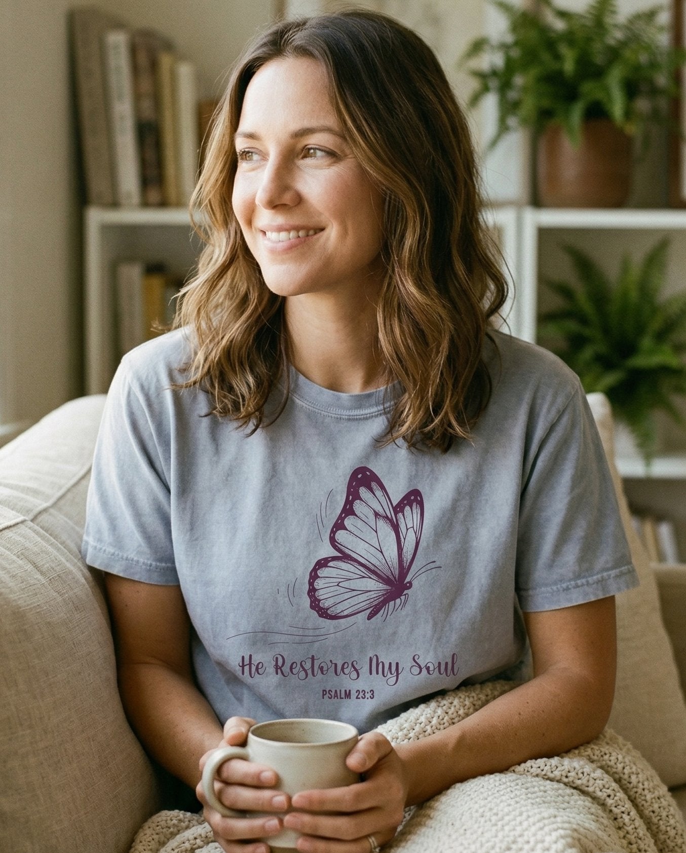 Restores My Soul Butterfly T-shirt – Granite women's Christian tee, lifestyle photo in cozy living room – A large detailed monarch butterfly illustration in deep purple above s – Psalm 23:3 – She Wears Faith