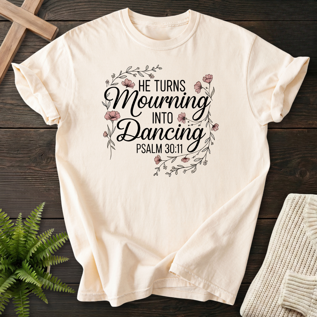 Ivory women's Christian t-shirt with a decorative flower wreath and "He Turns Mourning Into Dancing" script