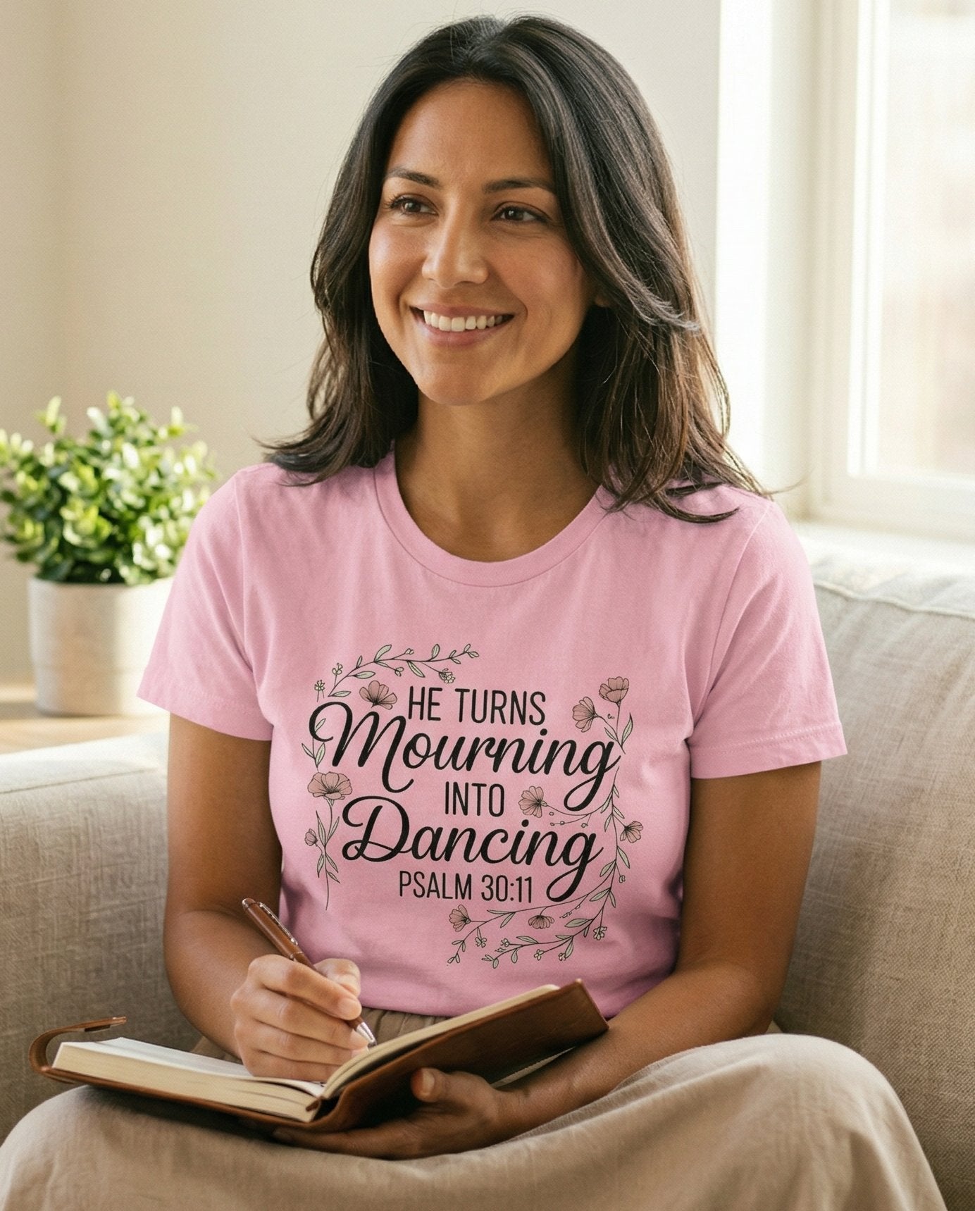 Mourning Into Dancing – Blossom women's Christian tee, lifestyle photo in cozy living room – Decorative floral wreath framing bold script 'He Turns Mourning Into D – Psalm 30:11 – She Wears Faith