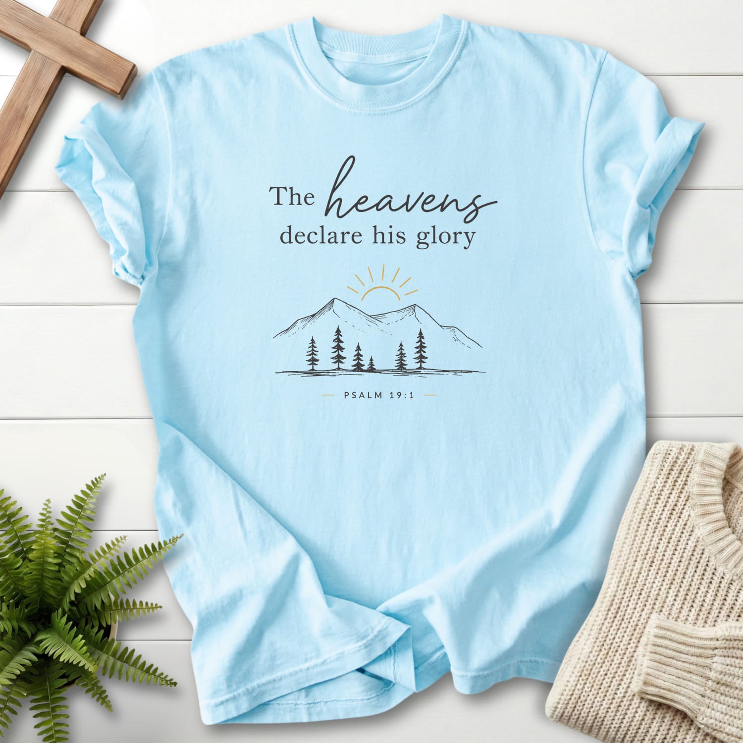 Flat lay of a Chambray faith-inspired shirt featuring sunrise graphic with "Heavens Declare His Glory Dark T-Shirt" Psalm 19:1.
