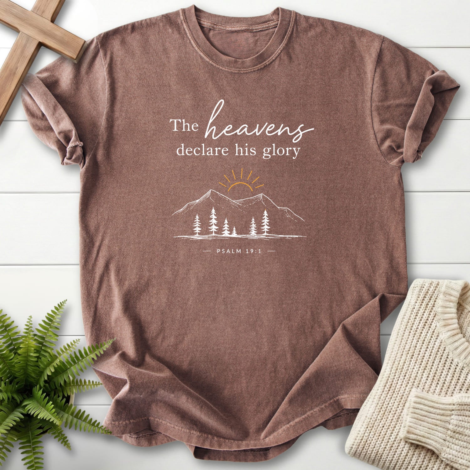 Flatlay of an Espresso Christian shirt with sunrise graphic with "Heavens Declare His Glory Dark T-Shirt" Psalm 19:1.