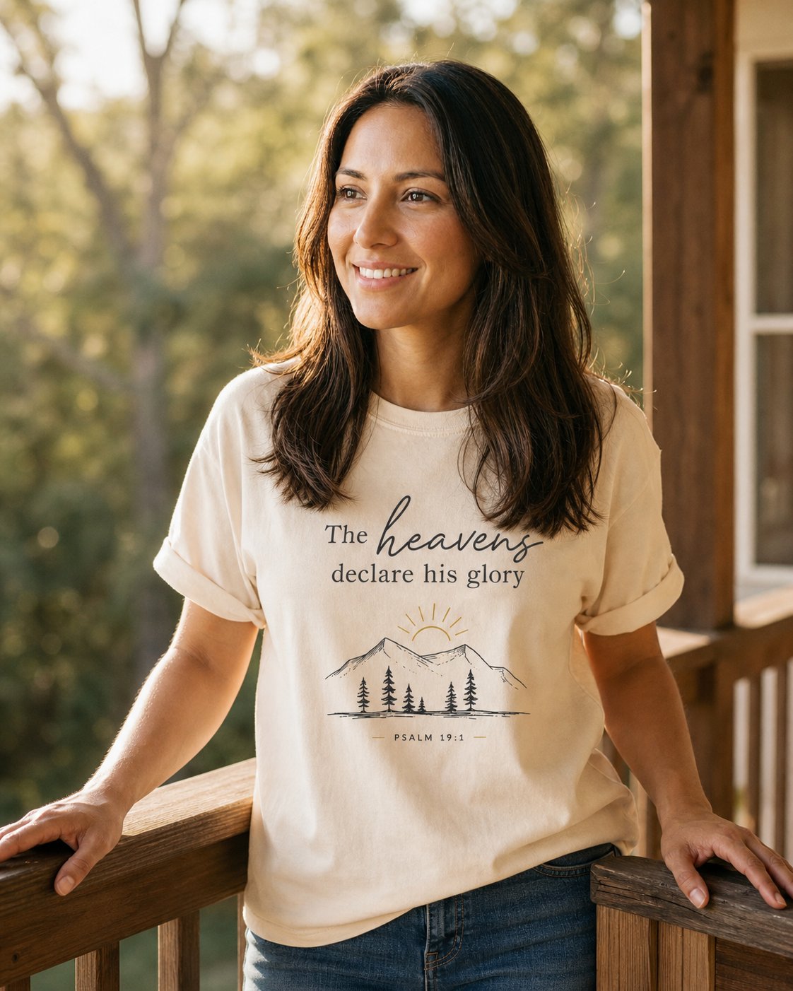 Heavens Declare His Glory – Ivory women's Christian tee, lifestyle photo in sunny porch – Line-art sunrise over mountains and pine trees – Psalm 19:1 – She Wears Faith