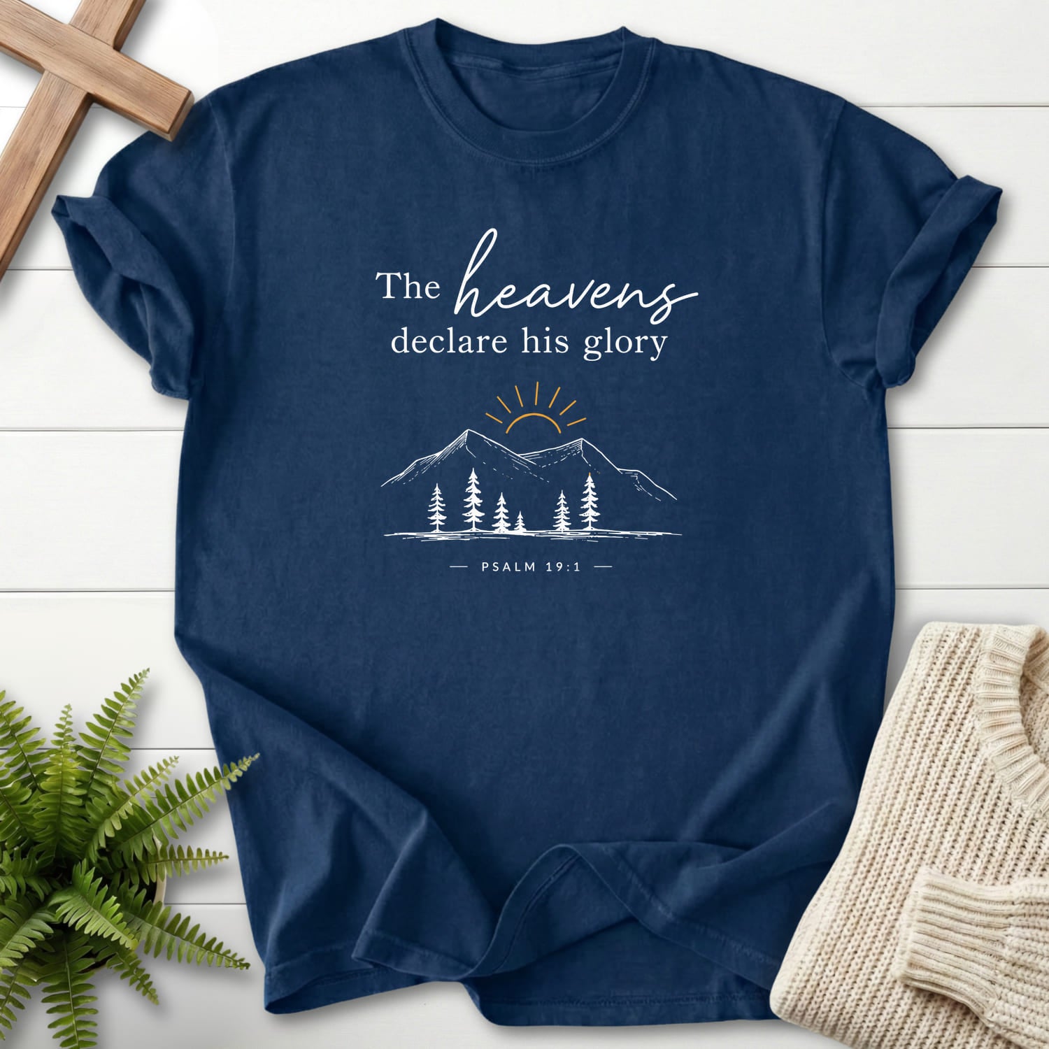 Flatlay of a Navy Scripture shirt with sunrise graphic with "Heavens Declare His Glory Dark T-Shirt" Psalm 19:1.
