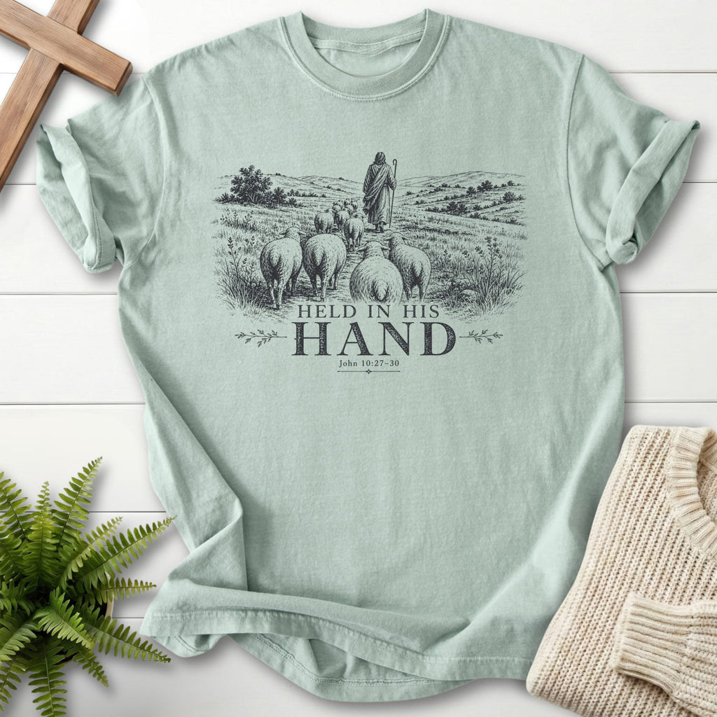Flat lay of a Bay Scripture shirt featuring "Held in His Hand T-Shirt" John 10:27-30.