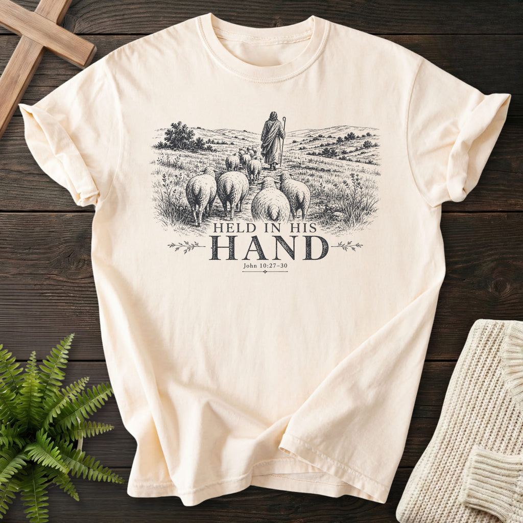 Flat lay of an Ivory Comfort Colors 1717 garment-dyed Christian tee featuring "Held in His Hand T-Shirt" John 10:27-30.