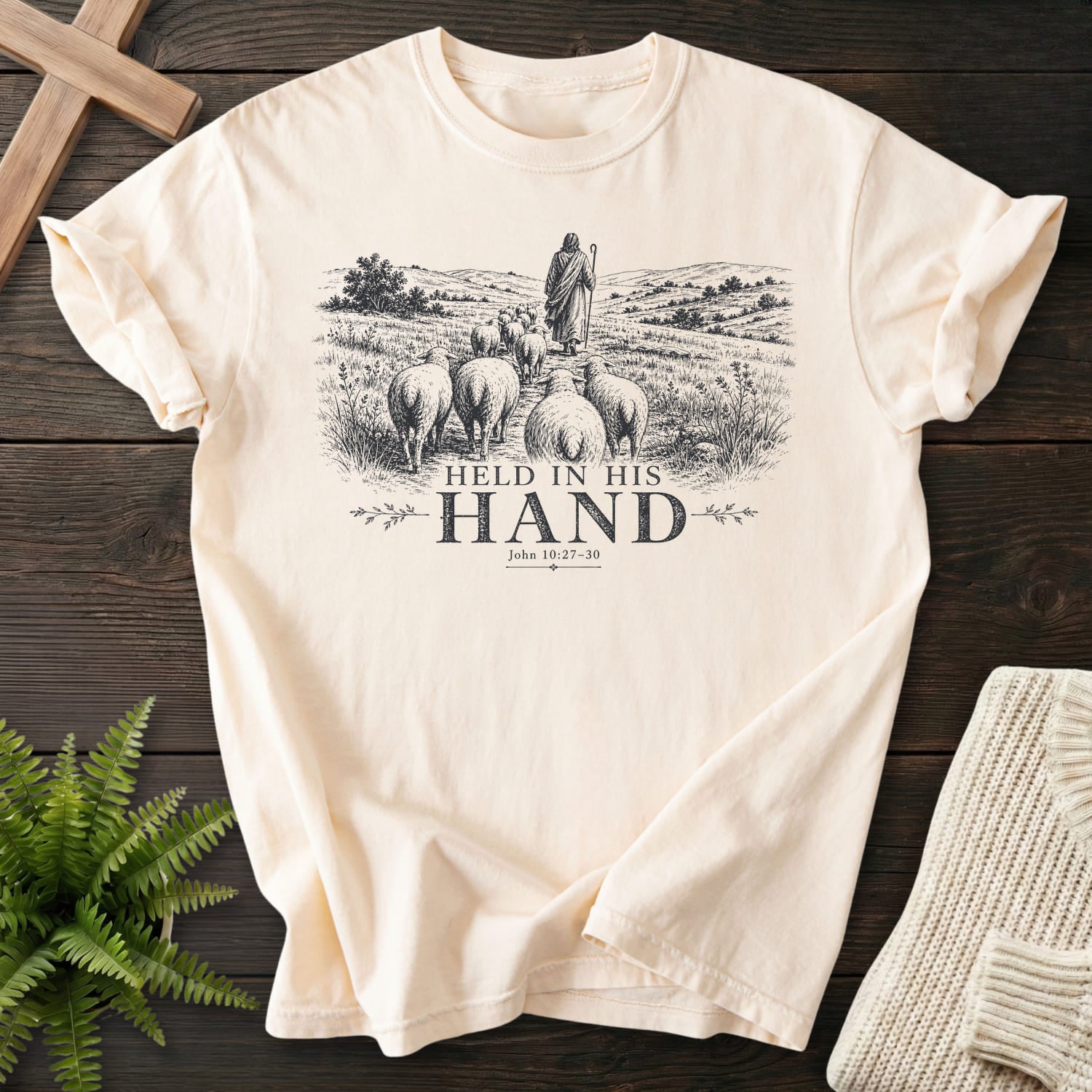 Flat lay of an Ivory Comfort Colors 1717 garment-dyed Christian tee featuring "Held in His Hand T-Shirt" John 10:27-30.