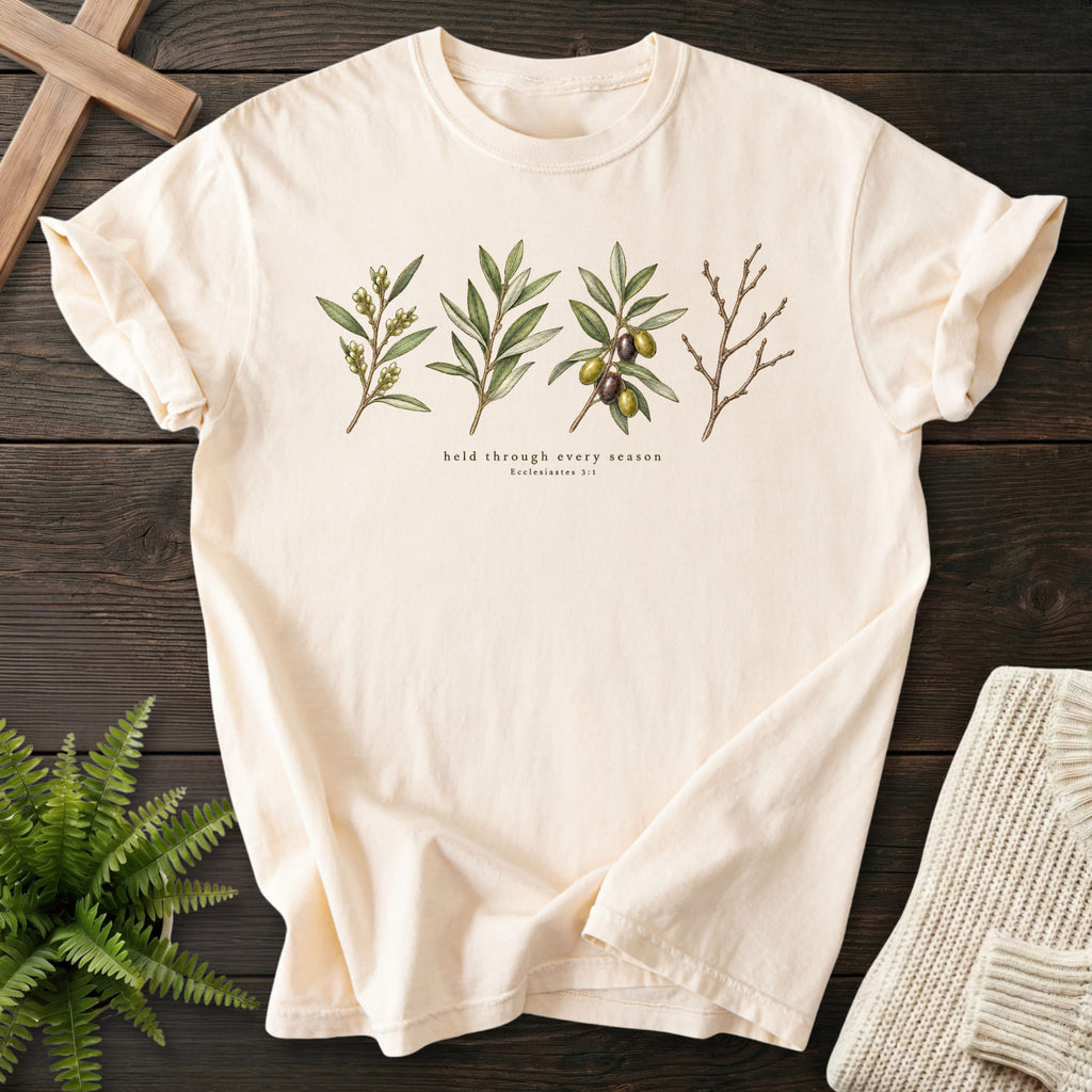 Flat lay of an Ivory Comfort Colors 1717 faith-inspired shirt featuring flower artwork with "Held Through Every Season T-Shirt" Ecclesiastes 3:1.