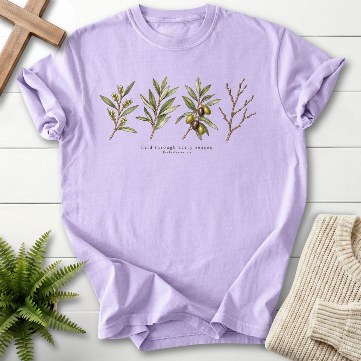 Flatlay of an Orchid Christian shirt with flower artwork with "Held Through Every Season T-Shirt" Ecclesiastes 3:1.