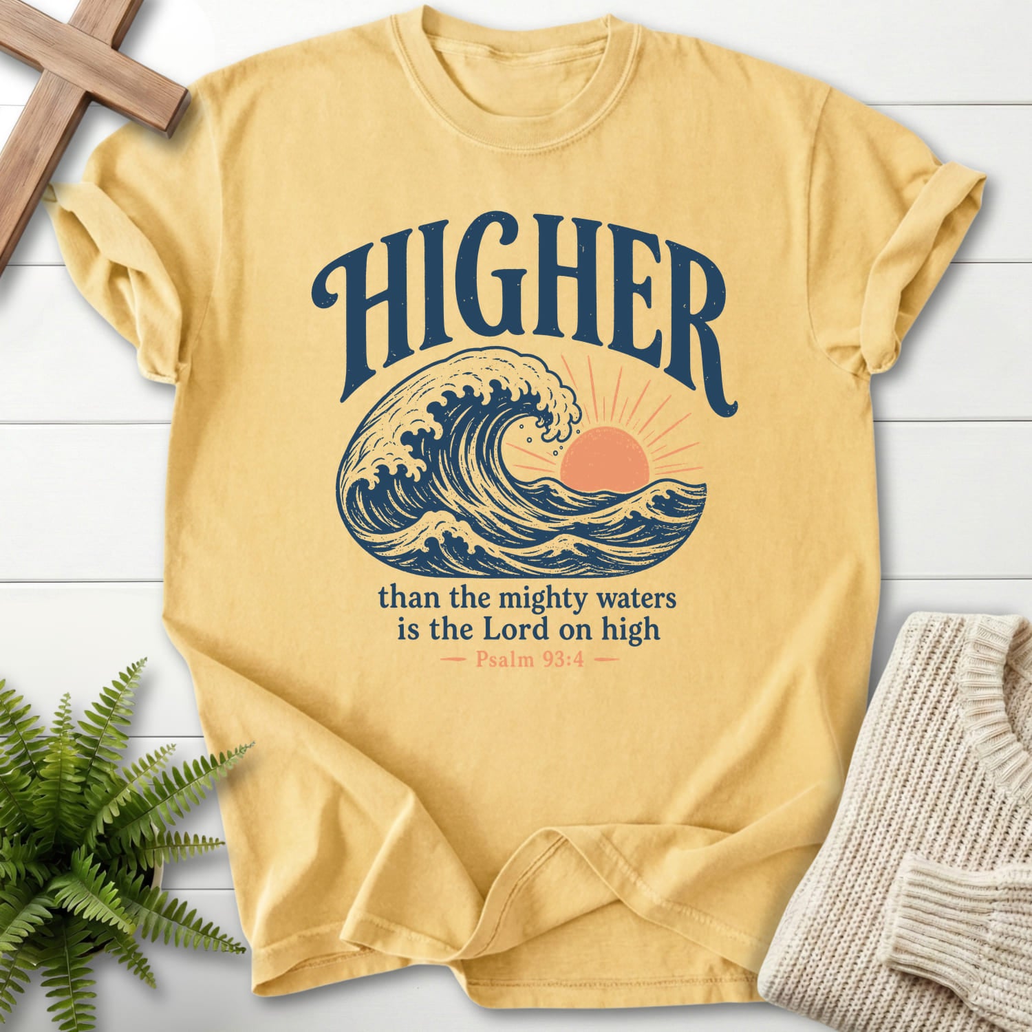 Flatlay of a Butter faith-inspired shirt with sunrise graphic with "Higher Than the Mighty Waters T-Shirt" From Printify.