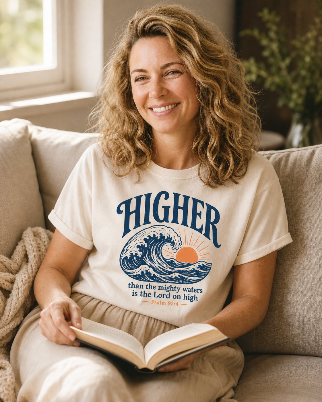 Higher Than the Mighty Waters – Ivory women's Christian tee, lifestyle photo in cozy living room – Woodblock cresting wave with an orange rising sun – Psalm 93:4 – She Wears Faith