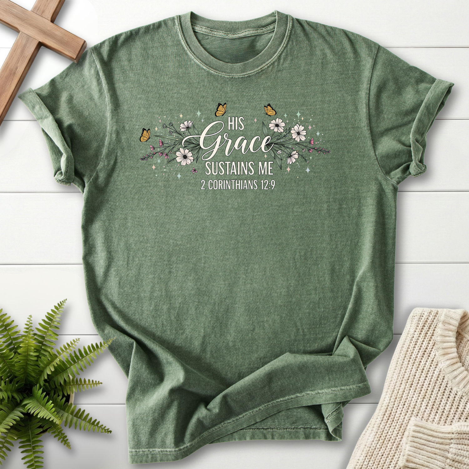 Moss women's Christian t-shirt with a floral garland, butterflies, and "His Grace Sustains Me," inspired by 2 Corinthians 12:9