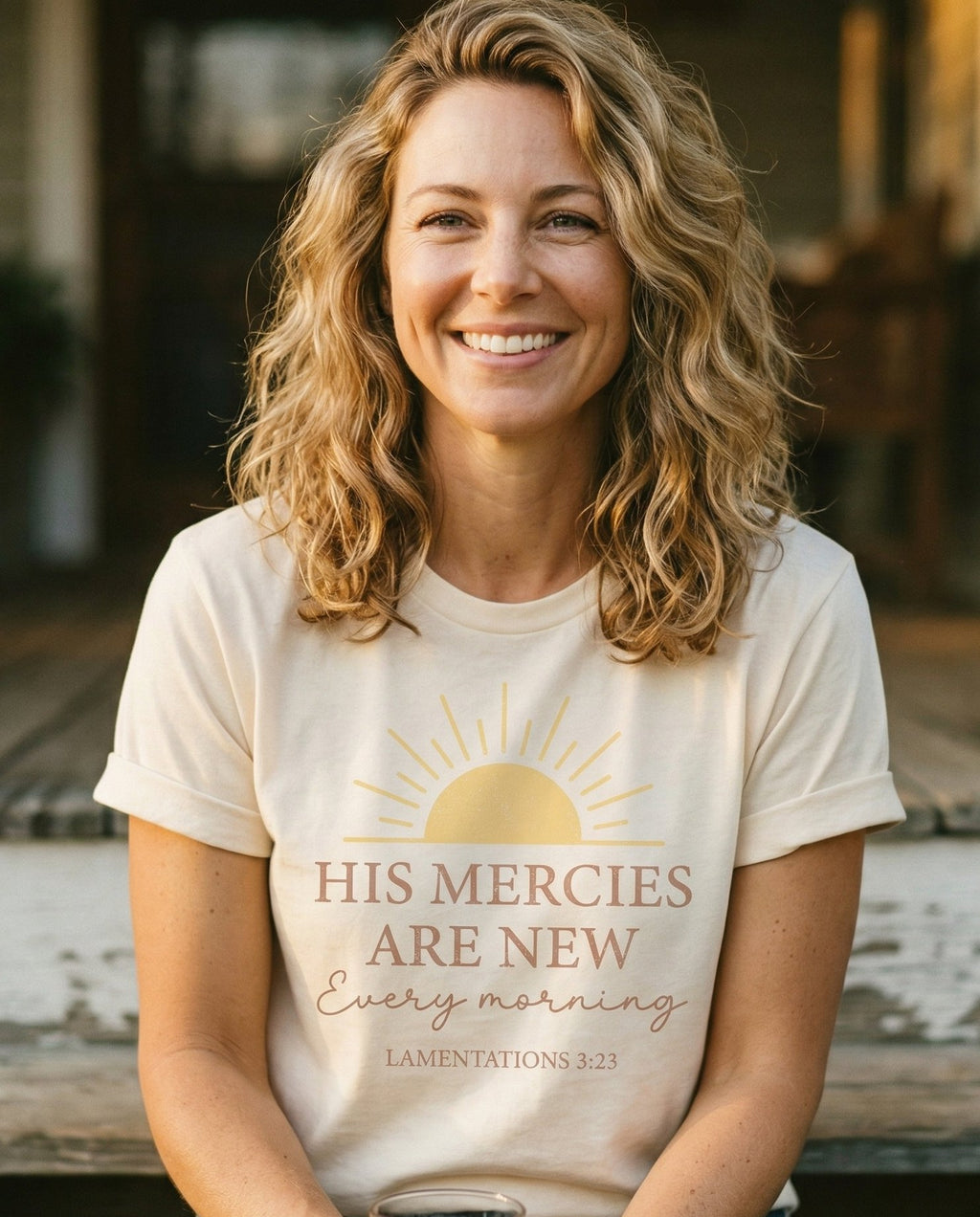 His Mercies – Ivory women's Christian tee, lifestyle photo in sunny porch – Rising sun illustration above bold and script lettering 'His Mercies A – Lamentations 3:23 – She Wears Faith