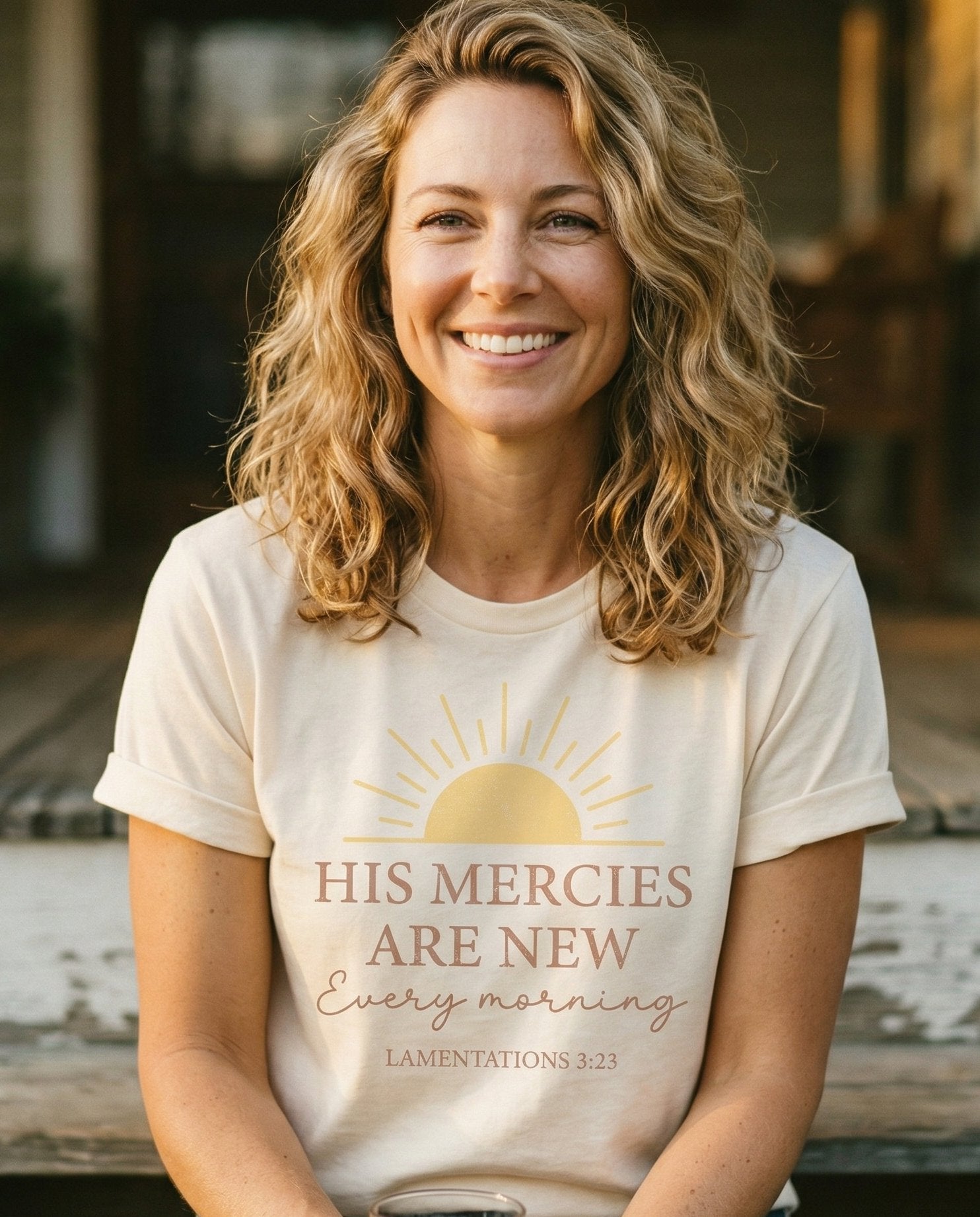 His Mercies – Ivory women's Christian tee, lifestyle photo in sunny porch – Rising sun illustration above bold and script lettering 'His Mercies A – Lamentations 3:23 – She Wears Faith