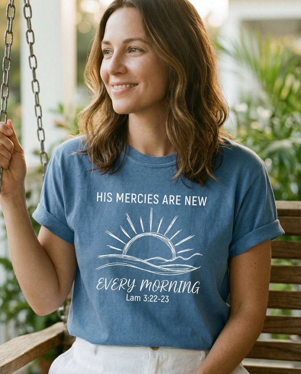 His Mercies Are New Every Morning – Blue Jean women's Christian tee, lifestyle photo in sunny porch – Minimalist line-art sunrise over hills with 'His Mercies Are New Every – Lamentations 3:22-23 – She Wears Faith