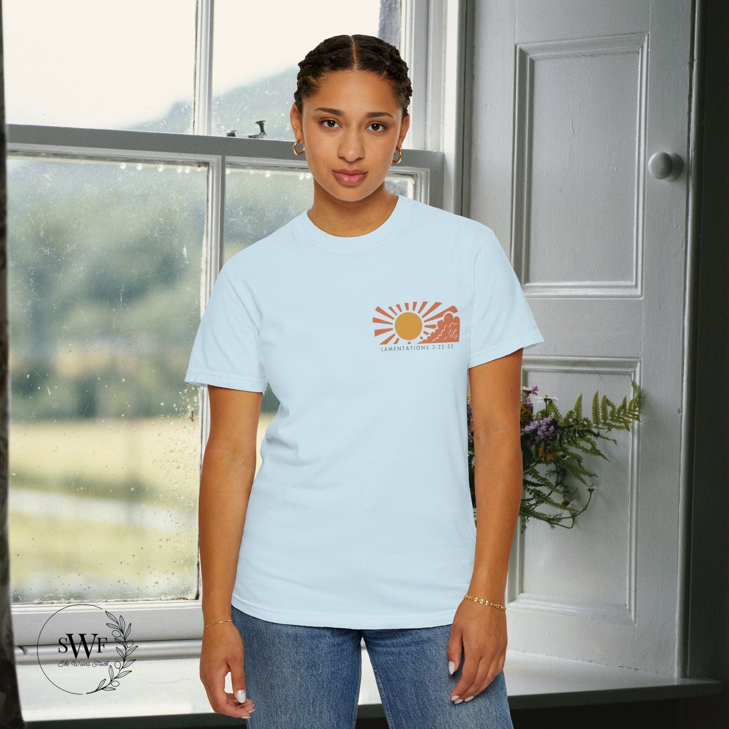 Person wearing a light blue t-shirt with a logo in a room with a window and door.