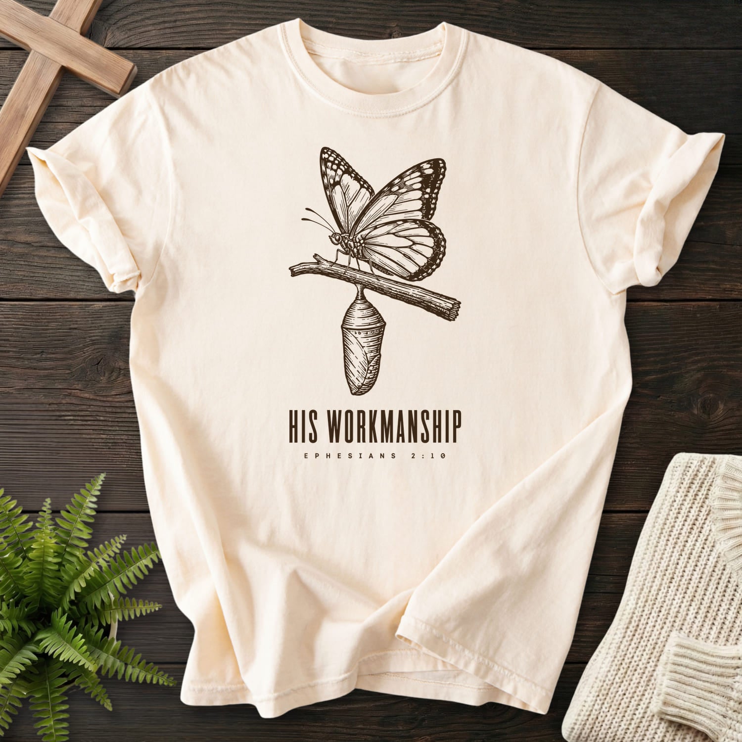 Flatlay of an Ivory faith-inspired shirt with butterfly artwork with "His Workmanship T-Shirt".