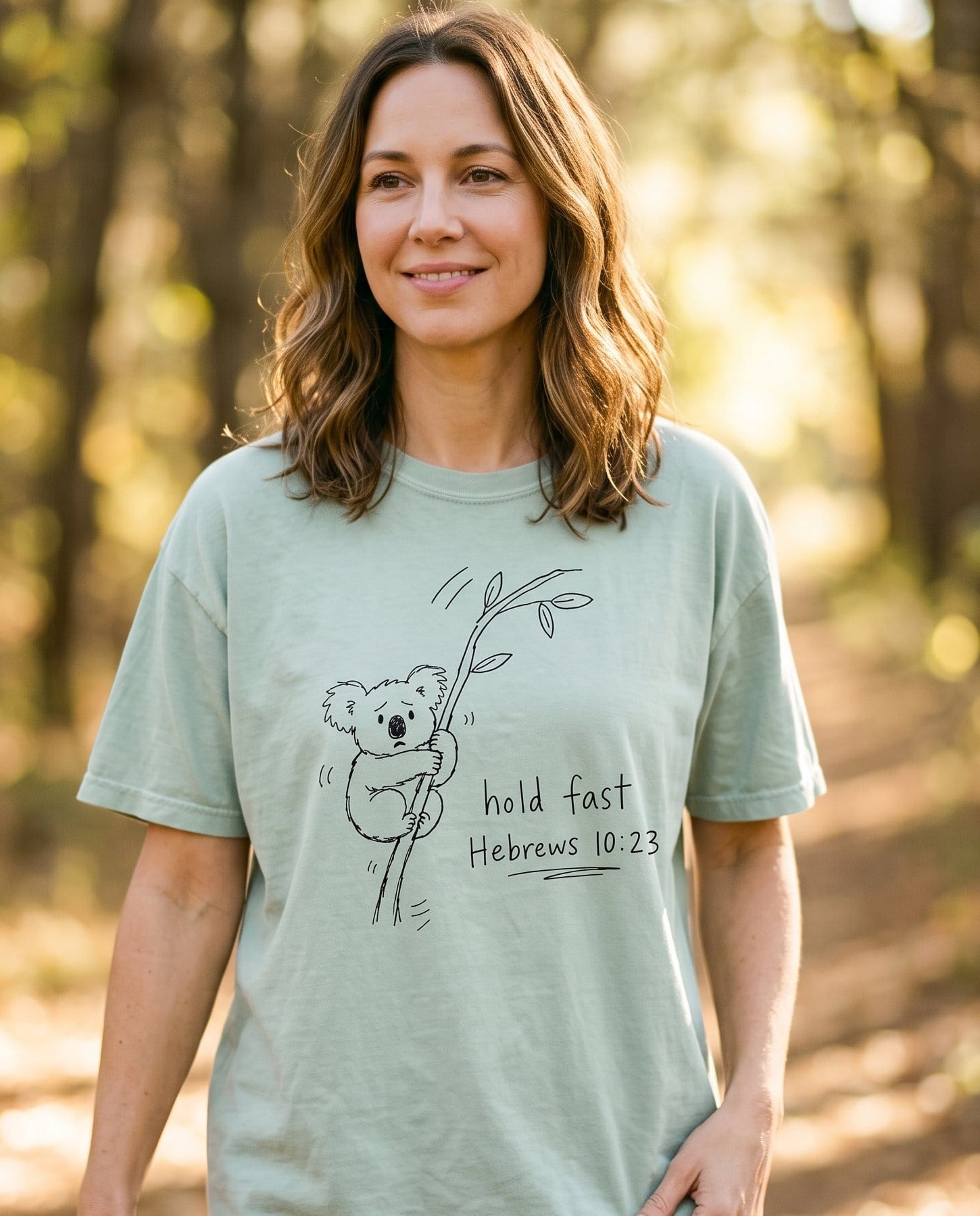 Hold Fast Hebrews 10:23 – Bay women's Christian tee, lifestyle photo in nature trail – Line-art koala climbing a eucalyptus branch beside handwritten "hold f – Hebrews 10:23 – She Wears Faith