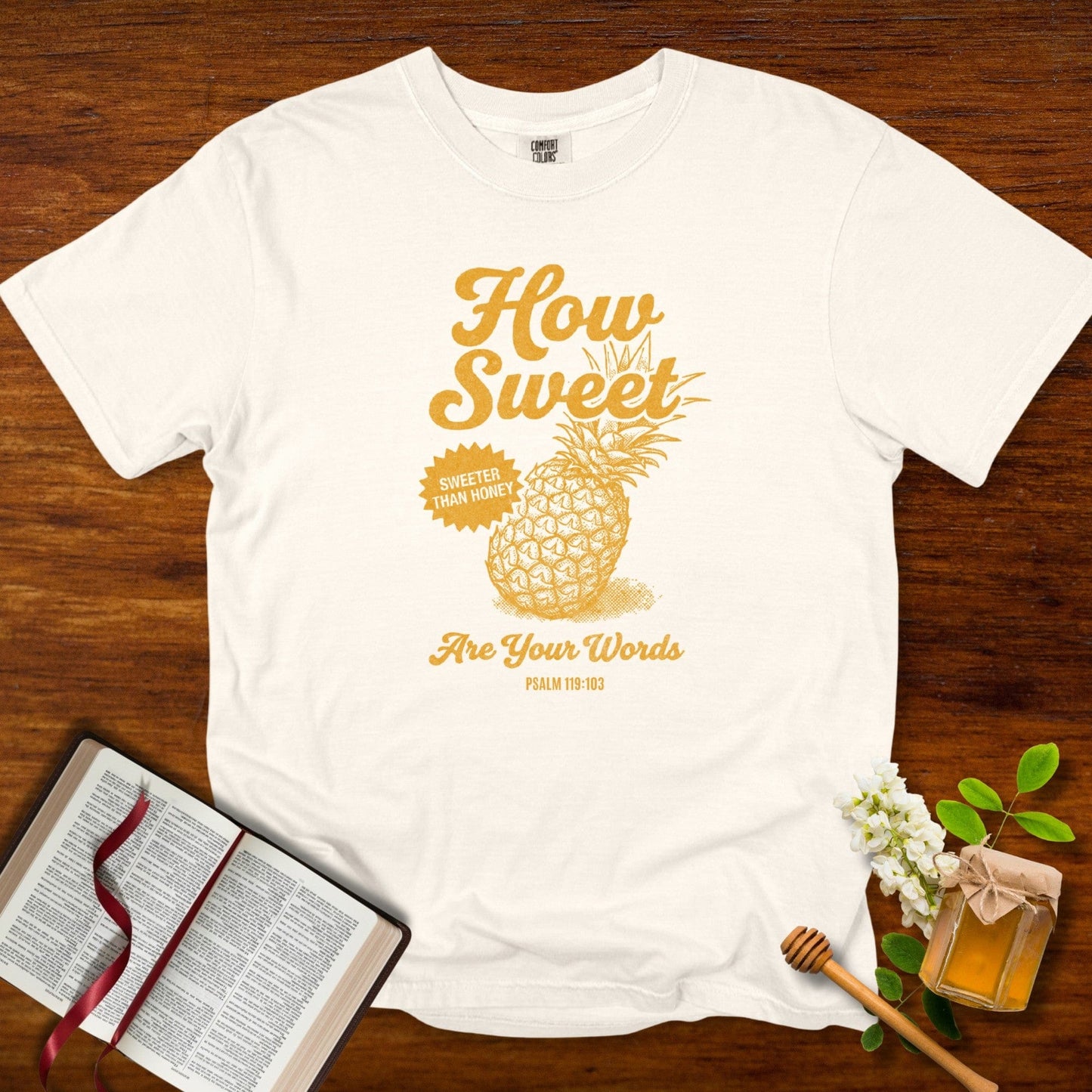 Faith-based “How Sweet Are Your Words” Psalm 119:103 tshirt for Christian women, printed in golden ink on an ivory Comfort Colors 1717 tee, displayed with Bible and honey props; inspirational US faith wear.