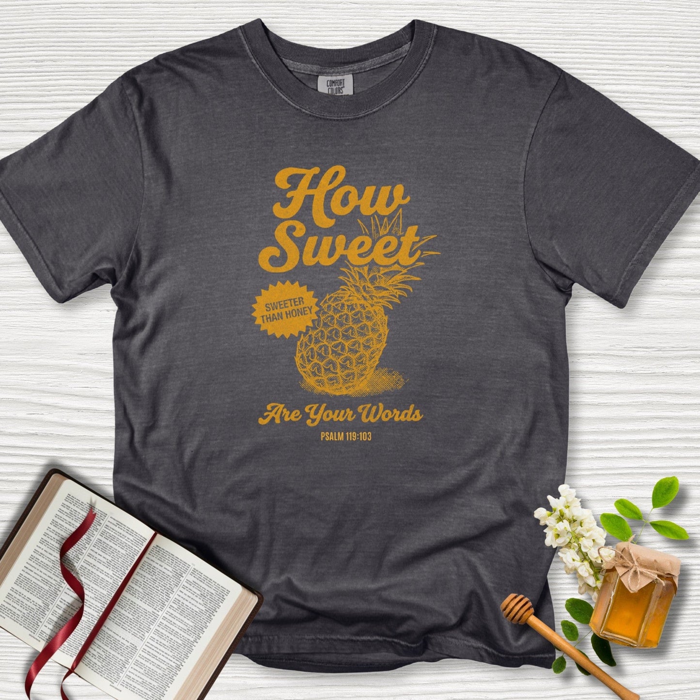 Christian women tshirt in pepper Comfort Colors 1717 featuring a vintage pineapple graphic and Psalm 119:103 “How Sweet Are Your Words,” styled with Bible and honey elements; US faith wear apparel.