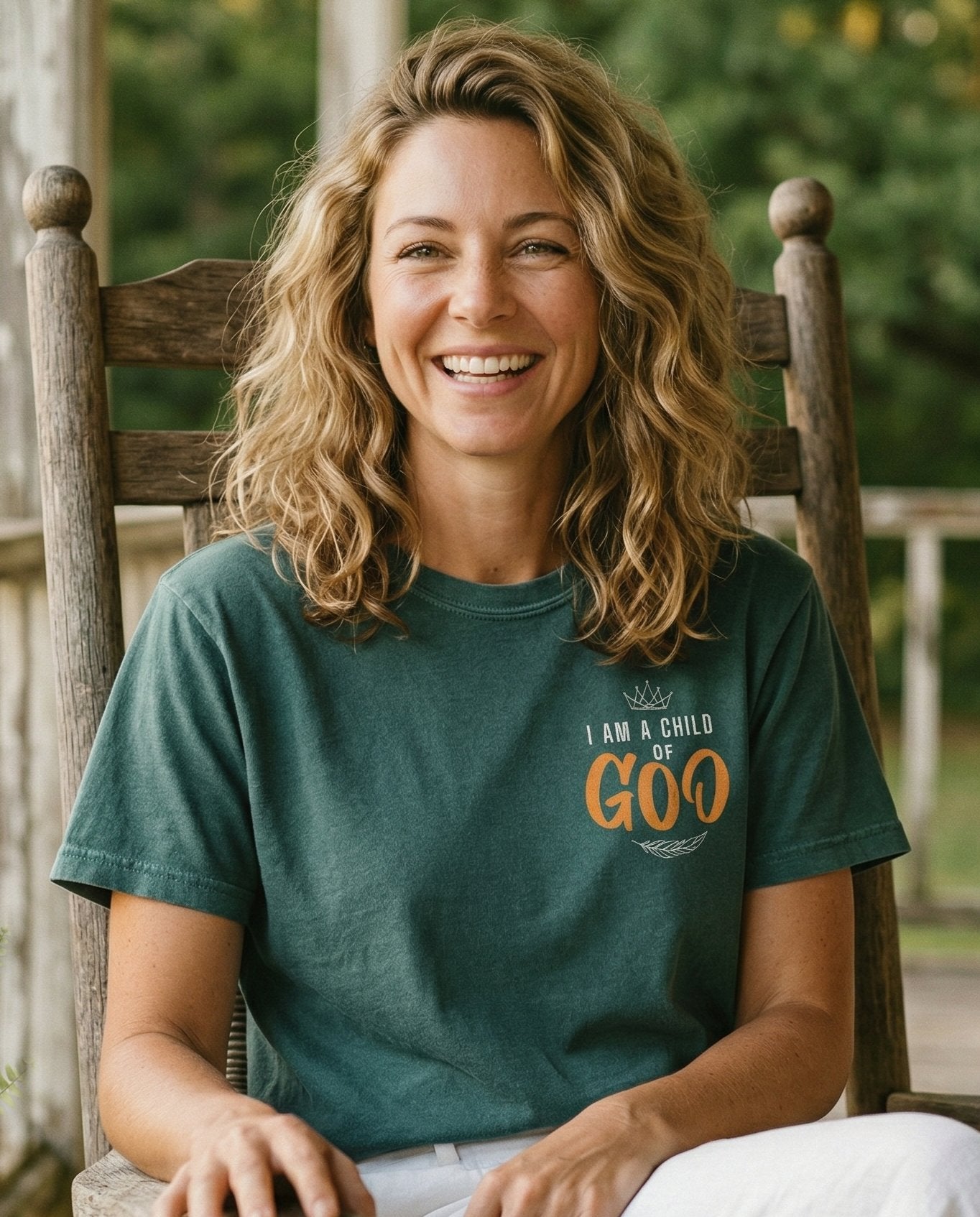 Child of God T-shirt – Blue Spruce women's Christian tee, lifestyle photo in sunny porch – Small left-chest pocket design with a crown at top – She Wears Faith