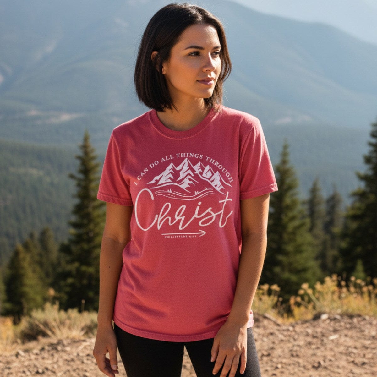 Woman standing in a mountain landscape wearing a Comfort Colors 1717 crimson “I Can Do All Things Through Christ – Philippians 4:13” t-shirt. A bold women’s scripture tee for faith-filled adventure and encouragement.