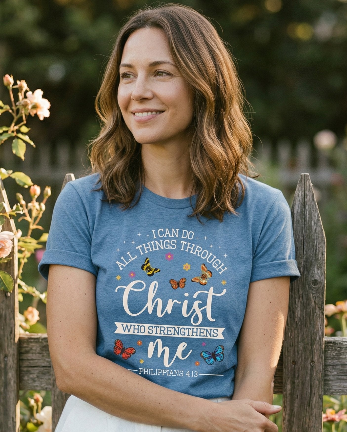 Do All Things Through Christ – Blue Jean women's Christian tee, lifestyle photo in outdoor garden – Colorful butterfly illustrations surrounding 'I Can Do All Things Thro – Philippians 4:13 – She Wears Faith