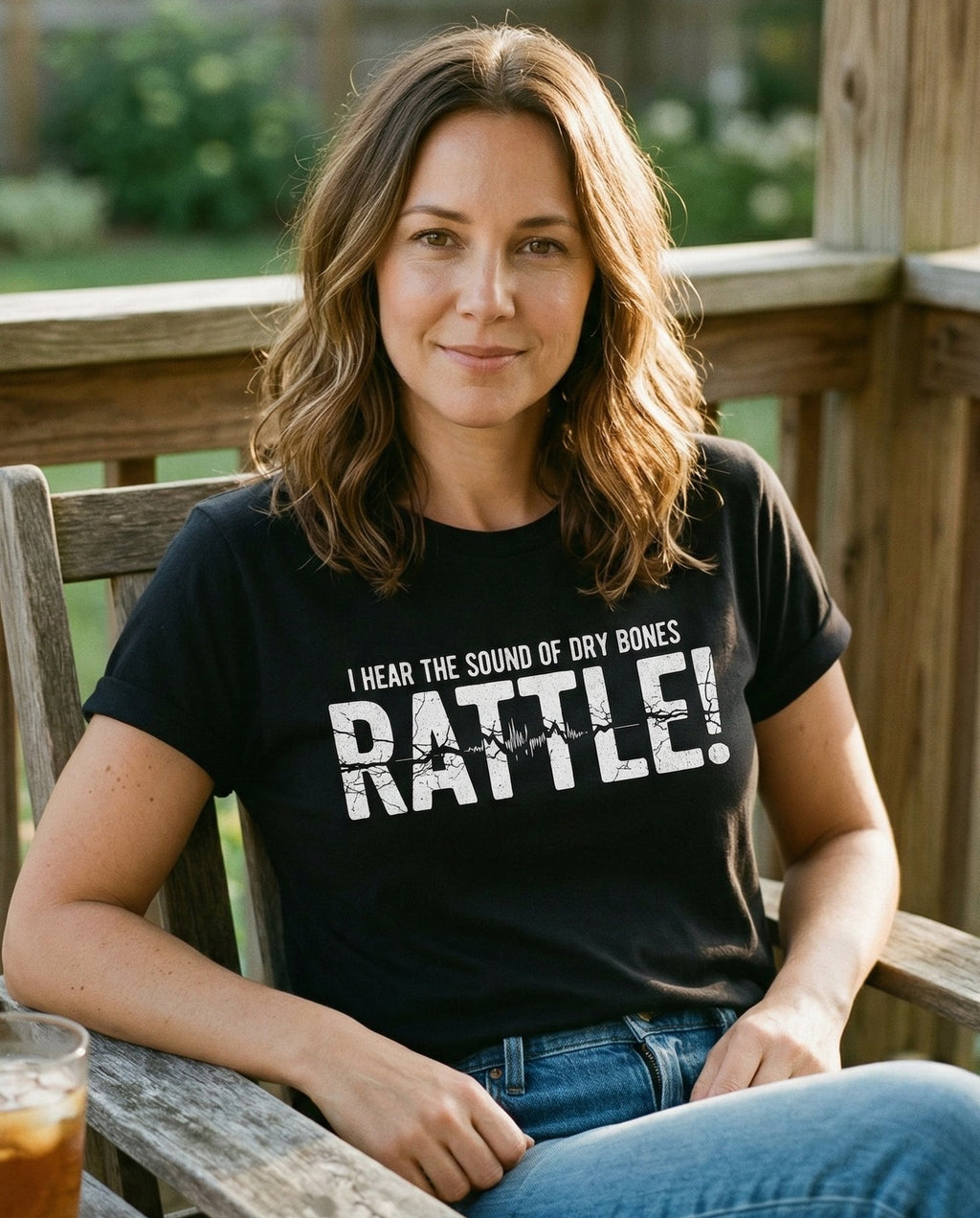 Dry Bones Rattle! T-shirt – Black women's Christian tee, lifestyle photo in sunny porch – Bold distressed-type design reading 'I Hear the Sound of Dry Bones RAT – She Wears Faith