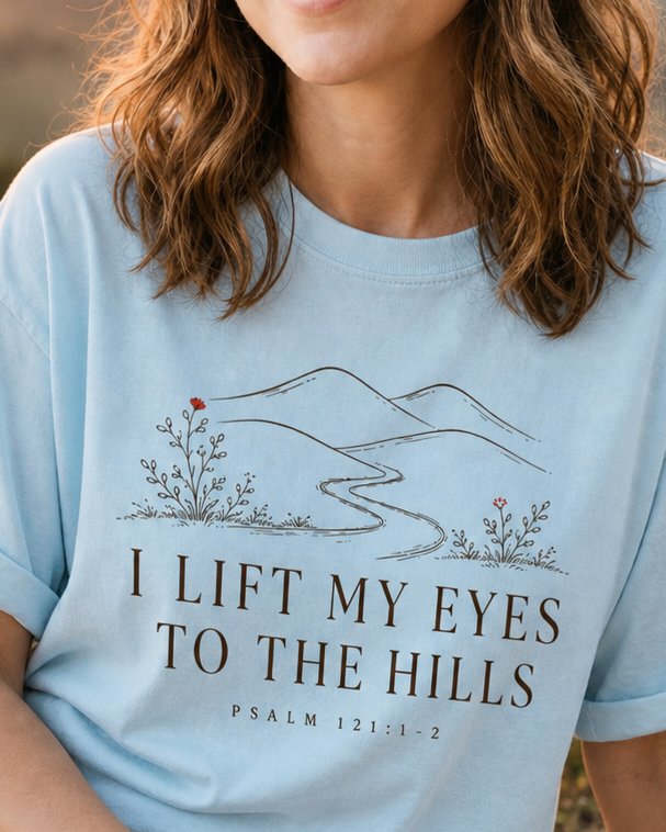 I Lift My Eyes to the Hills - Chambray women's Christian tee, lifestyle photo in wildflower meadow at sunrise - Line-art rolling hills with a winding path and wildflowers - Psalm 121:1-2 - She Wears Faith