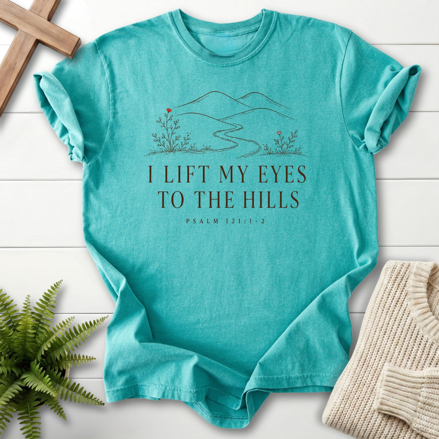 Flat lay of a Seafoam Scripture shirt featuring floral line art with "I Lift My Eyes to the Hills T-Shirt" Psalm 121:1-2.