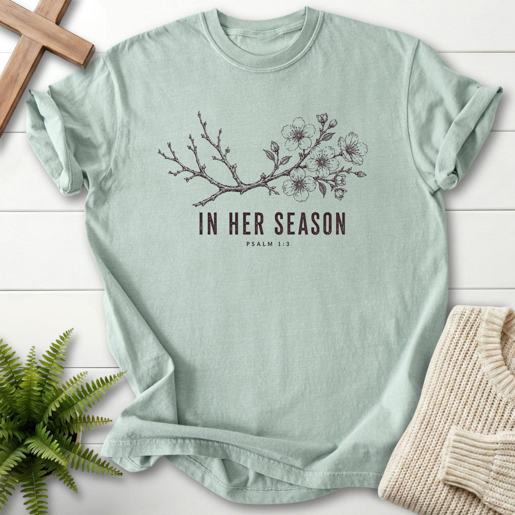 Flat lay of a Bay women's Christian tee featuring flowering branch artwork with "In Her Season T-Shirt" Psalm 1:3.