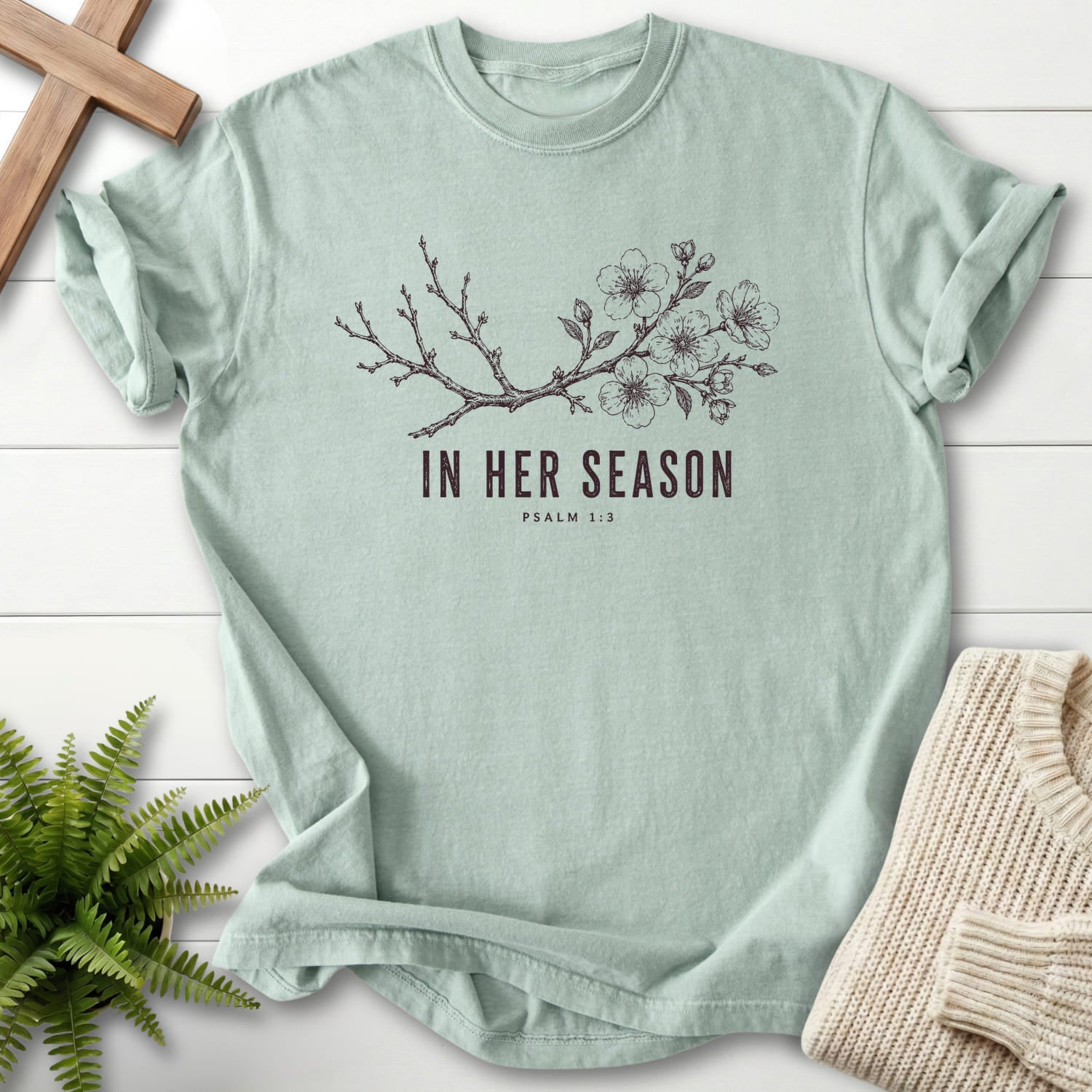 Flat lay of a Bay women's Christian tee featuring flowering branch artwork with "In Her Season T-Shirt" Psalm 1:3.