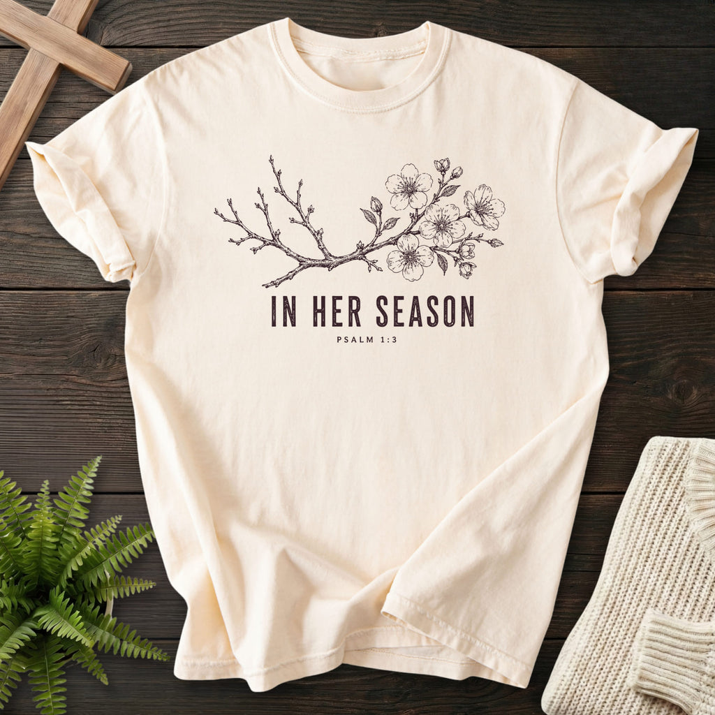 Flatlay of an Ivory faith-based tee with flowering branch artwork with "In Her Season T-Shirt" Psalm 1:3.