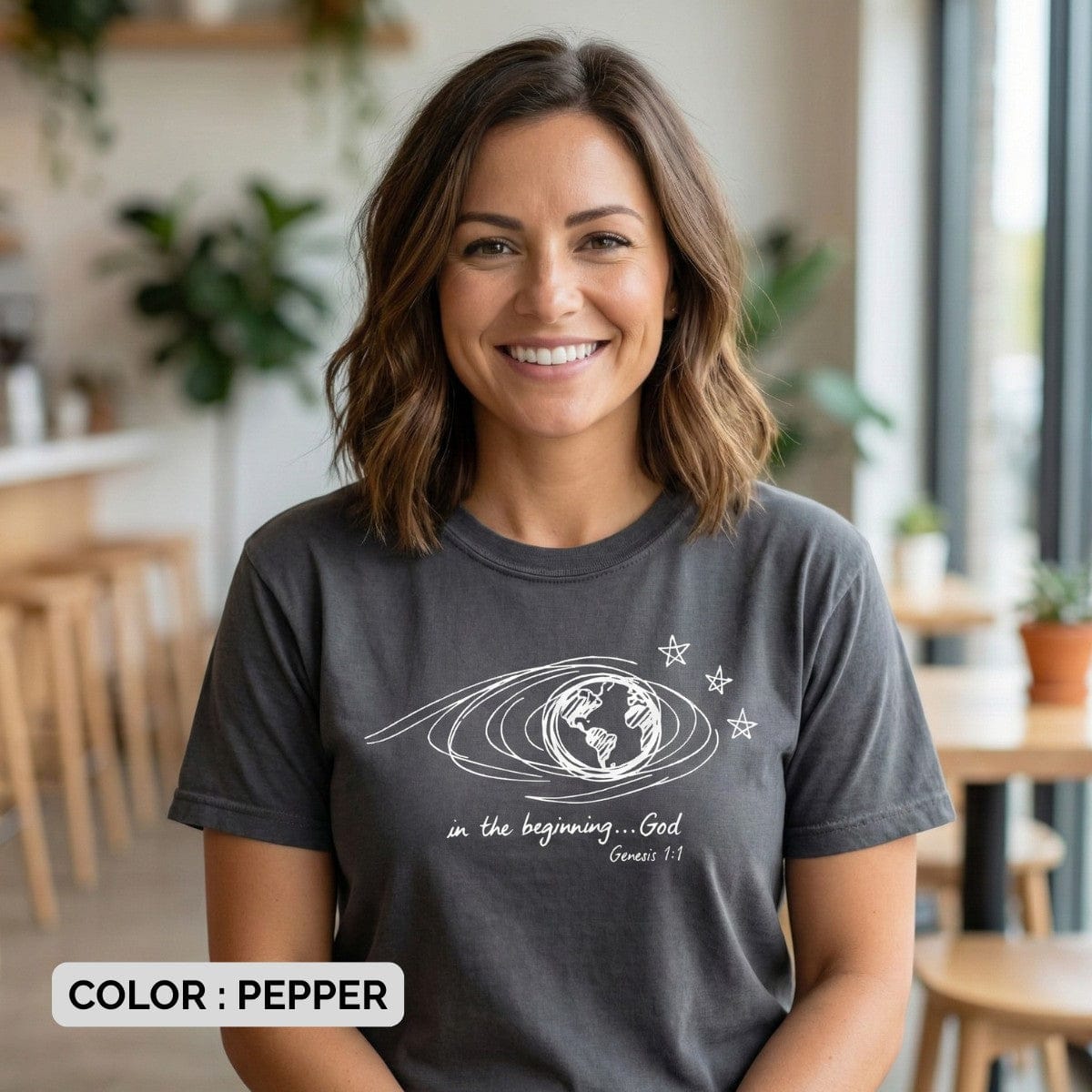 Smiling model wearing a Pepper Grey Comfort Colors 1717 tshirt with a Genesis 1:1 scripture design. Casual Christian women tee styling featuring naive art, showcasing trendy US faith wear for women.