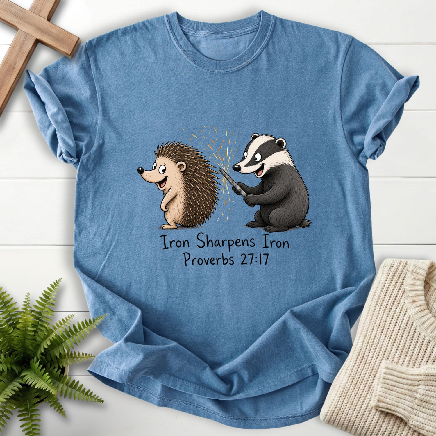 Flatlay of a Blue Jean Christian t-shirt for women with "Iron Sharpens Iron Proverbs 27:17 T-Shirt" Proverbs 27:17 From Printify.