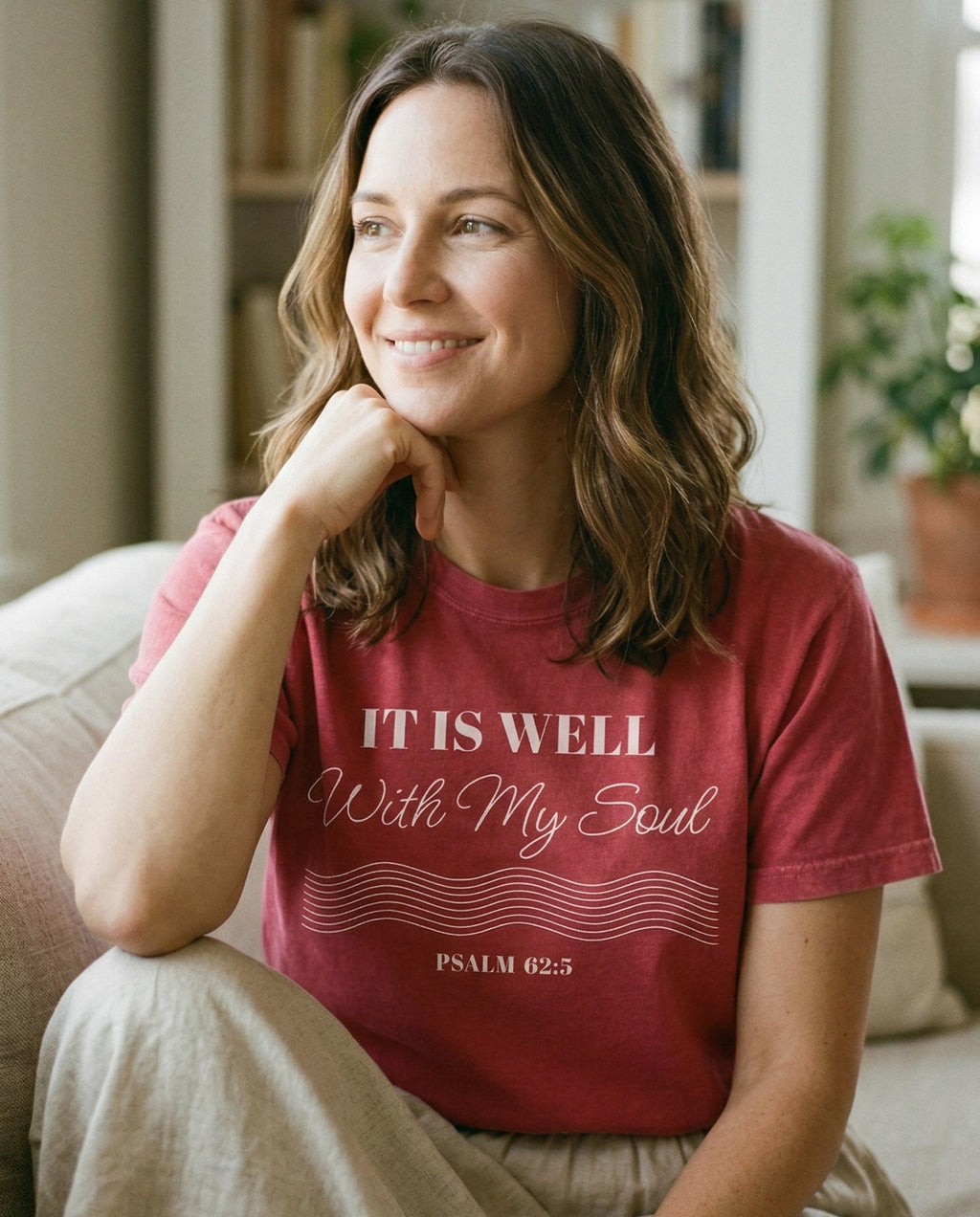 It Is Well With My Soul – Crimson women's Christian tee, lifestyle photo in cozy living room – Elegant serif and script typography reading 'It Is Well With My Soul'  – Psalm 62:5 – She Wears Faith