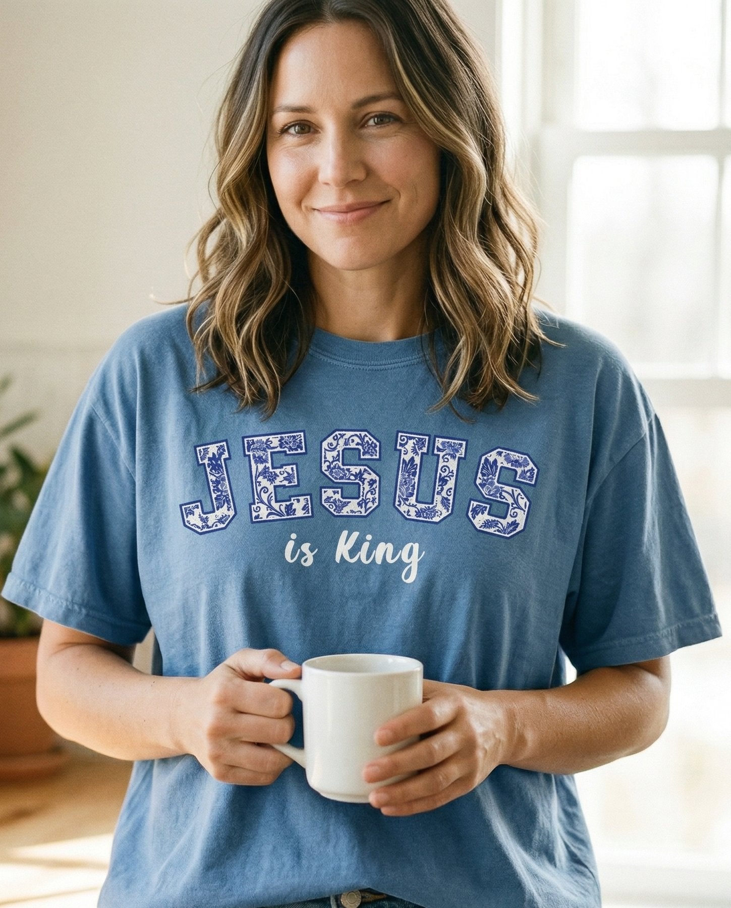 Jesus is King Floral – Blue Jean women's Christian tee, lifestyle photo in morning kitchen setting – Collegiate varsity block letters spelling 'JESUS' filled with a blue f – She Wears Faith