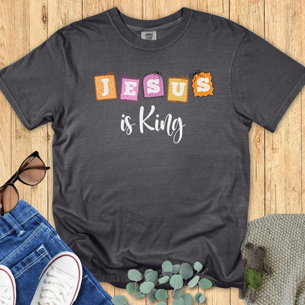Flatlay of a Comfort Colors 1717 pepper “Jesus is King” t-shirt with playful stitched block letters in orange, pink, and yellow. A soft women’s scripture tee -  faith-based apparel for women and modern Christian shirt, perfect Christian mom gift idea and Sunday outfit.