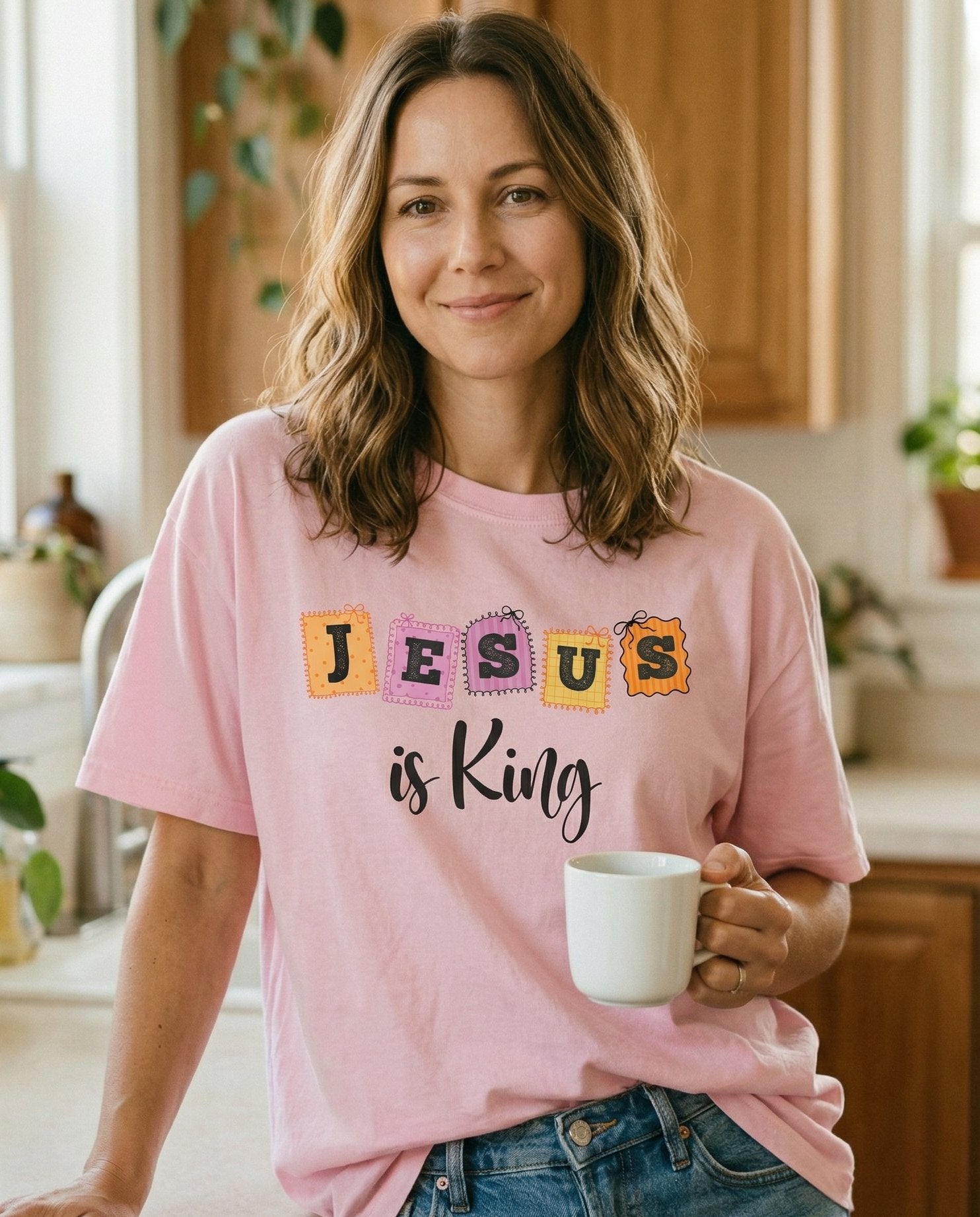 Jesus is King – Blossom women's Christian tee, lifestyle photo in morning kitchen setting – Whimsical patchwork-style design with 'JESUS' in colorful stamp letter – She Wears Faith