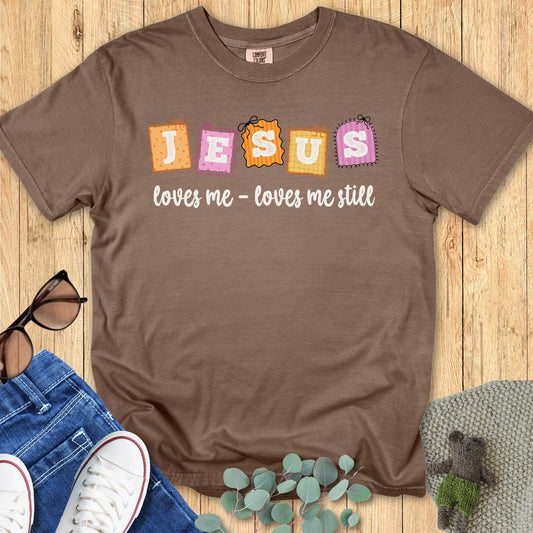 Flatlay of a Comfort Colors 1717 espresso brown “Jesus loves me – loves me still” t-shirt featuring bright stitched block letters. A cozy women’s scripture tee — faith-based apparel for women and modern Christian shirt, perfect Christian mom gift idea or teacher gift.
