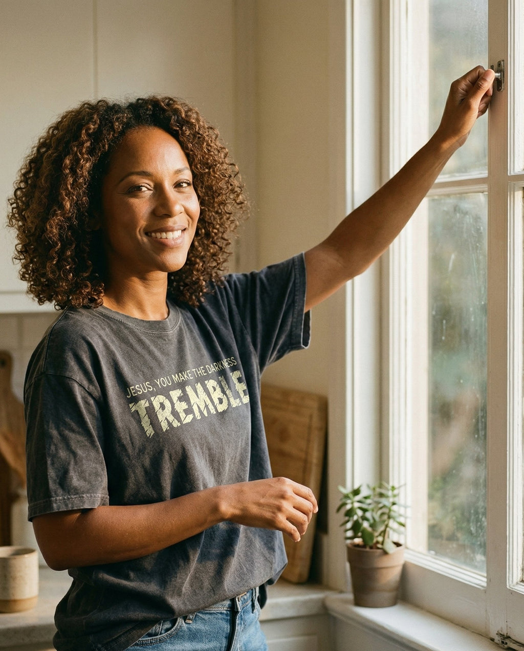 Darkness Must Tremble T-shirt – Pepper women's Christian tee, lifestyle photo in morning kitchen setting – Grunge chalk-textured typography reading 'Jesus – She Wears Faith
