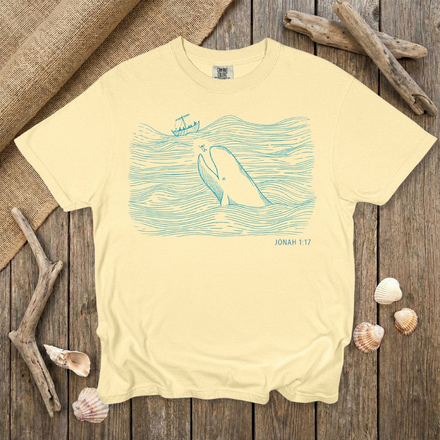 Comfort Colors 1717 butter yellow Christian women tee displaying a blue line-art illustration of Jonah and the great fish from Jonah 1:17. A bright and uplifting scripture-themed T-shirt designed for US faith wear and Christian women who enjoy playful Bible-story artwork.