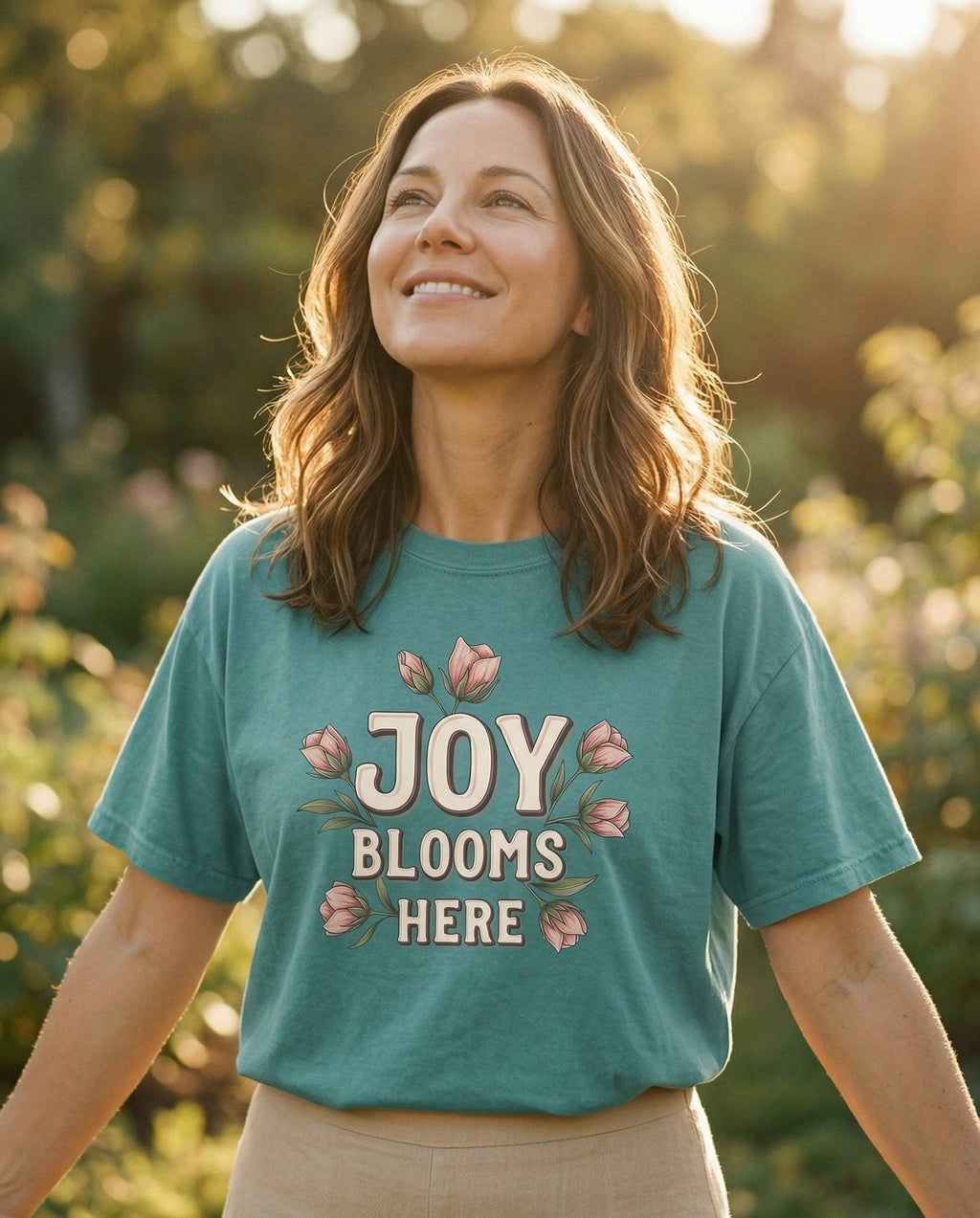 Joy Blooms Here T-shirt – Chalky Mint women's Christian tee, lifestyle photo in outdoor garden – Floral typography with 'JOY BLOOMS HERE' in retro block letters surrou – She Wears Faith