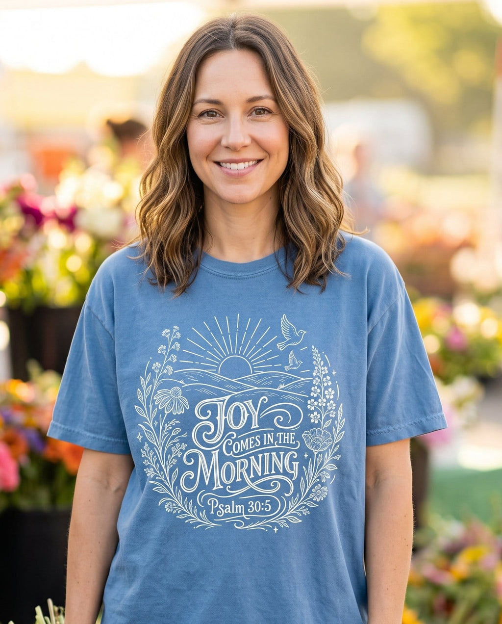 Joy Come In The Morning Wildflower – Blue Jean women's Christian tee, lifestyle photo in farmers market – Ornate script lettering "Joy Comes in the Morning" framed by wildflowe – Psalm 30:5 – She Wears Faith