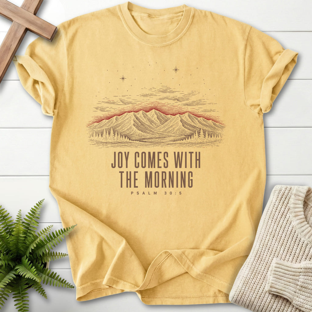 Flat lay of a Butter Comfort Colors 1717 Christian shirt featuring mountain graphic with "Joy Comes With the Morning Mountain T-Shirt" Psalm 30:5.