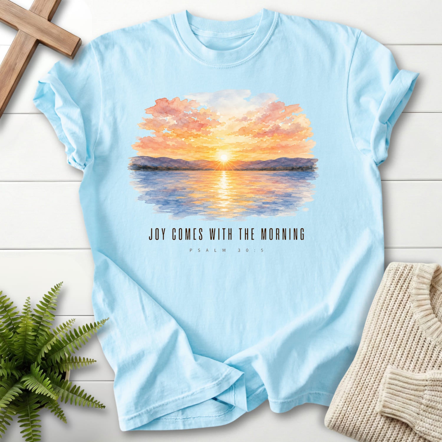 Flatlay of a Chambray faith-based tee with watercolor artwork with "Joy Comes With the Morning T-Shirt".