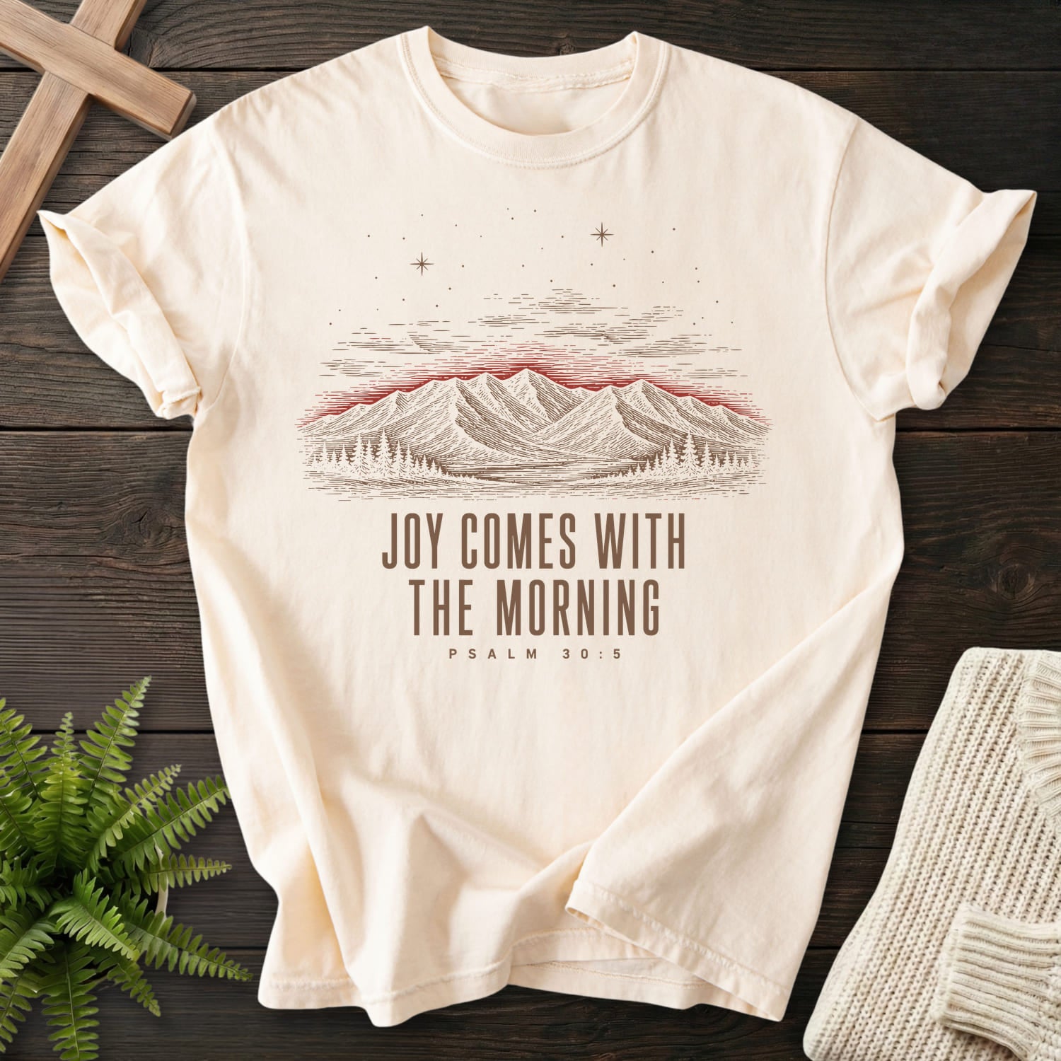 Flat lay of an Ivory Comfort Colors 1717 Scripture shirt featuring mountain graphic with "Joy Comes With the Morning Mountain T-Shirt" Psalm 30:5.