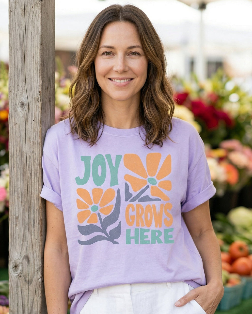 Joy Grows Here Floral – Orchid women's Christian tee, lifestyle photo in farmers market – Retro groovy design with 'JOY GROWS HERE' in teal and orange block let – She Wears Faith