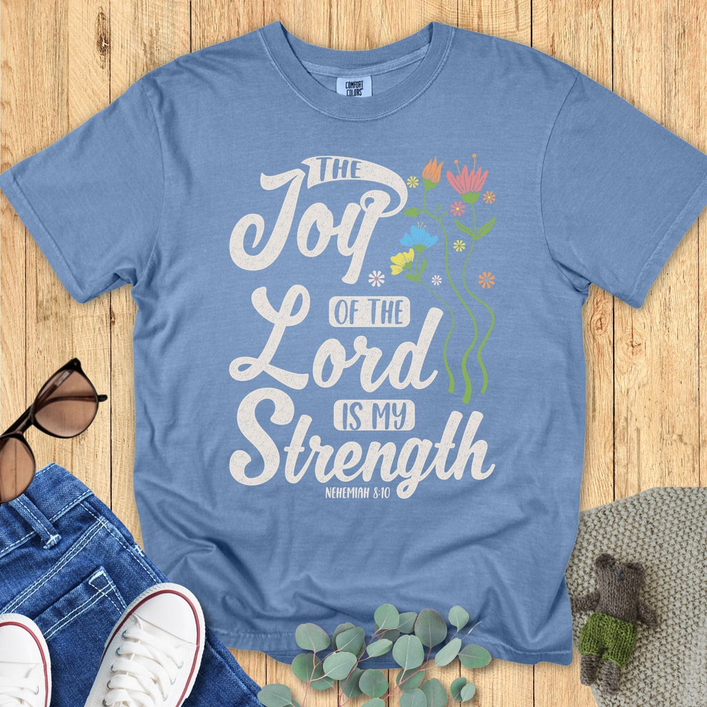 Comfort Colors 1717 Christian women’s t-shirt in blue jean, styled with denim, sunglasses, and greenery. Faith-inspired design includes flowers and the scripture “The Joy of the Lord is My Strength – Nehemiah 8:10