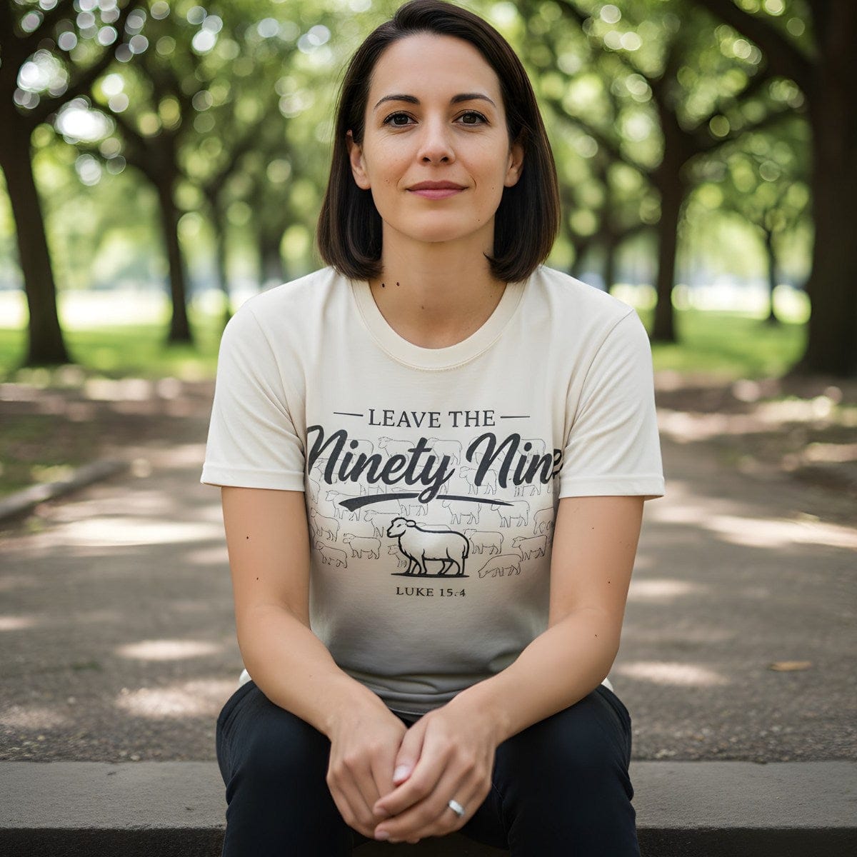 Woman sitting outdoors wearing a Comfort Colors 1717 ivory “Leave the Ninety-Nine – Luke 15:4” t-shirt featuring a shepherd and sheep design. A soft and meaningful women’s scripture tee — faith-based apparel for women and modern Christian shirt, perfect Christian mom gift idea.